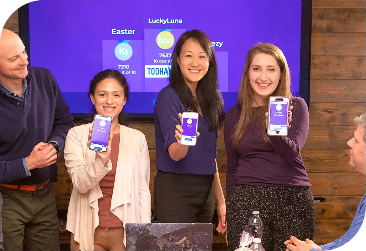 Three females smiling, holding mobile devices displaying the Kahoot podium