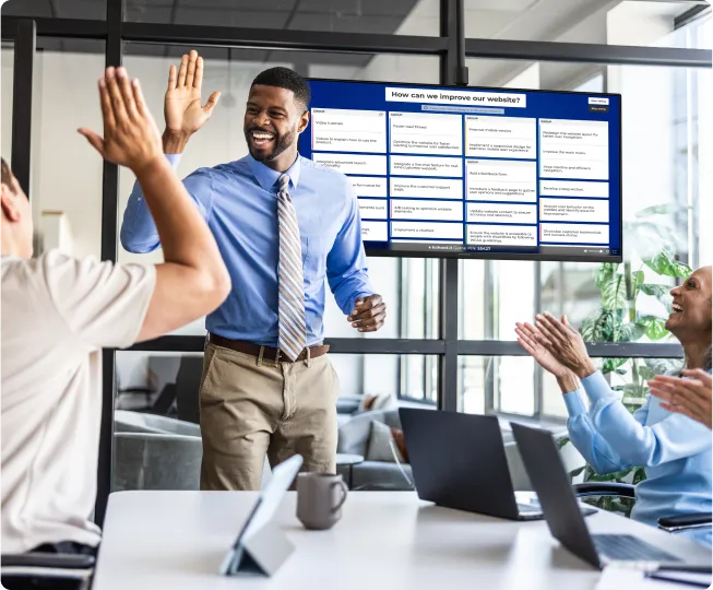 Facilitator high-fiving colleagues during a Kahoot brainstorming session displayed on an office meeting room screen