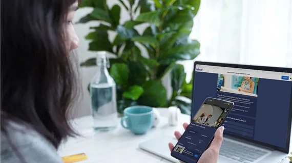 Woman accessing Kahoot on a smartphone and laptop while working from home at a bright desk