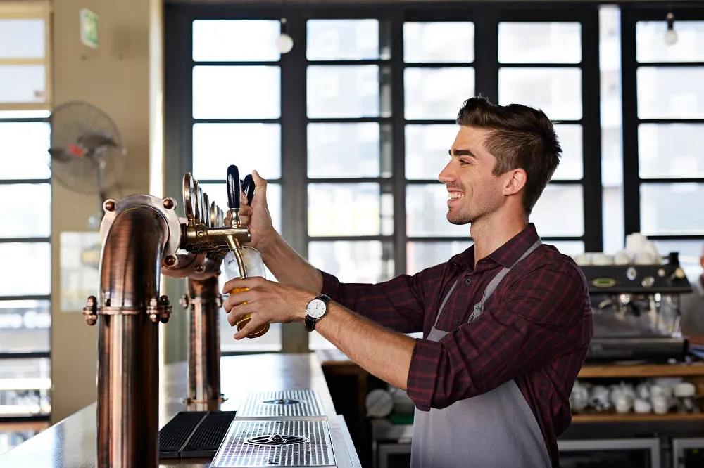 A smiling male bartender pouring a drink at a microbrewery