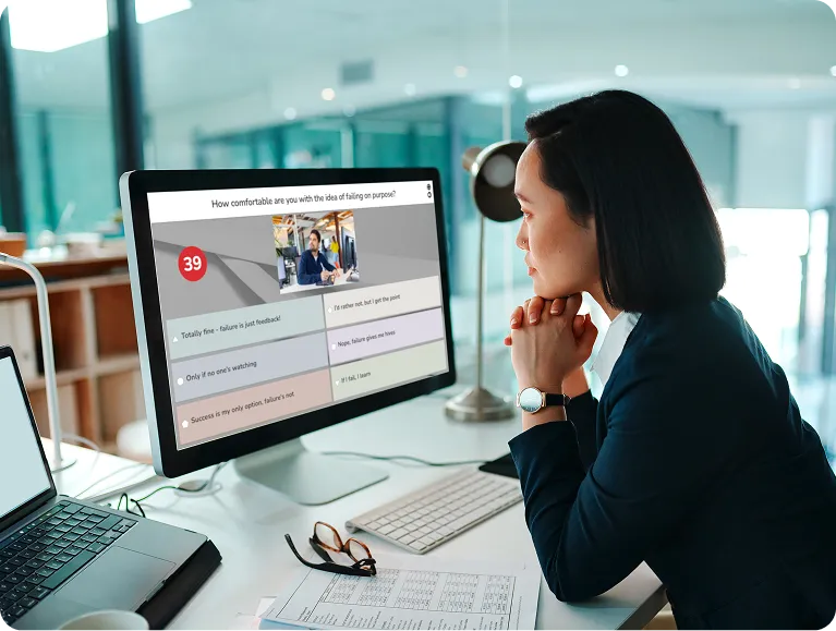 Woman thoughtfully viewing a Kahoot quiz question about failure on her desktop computer in a bright office