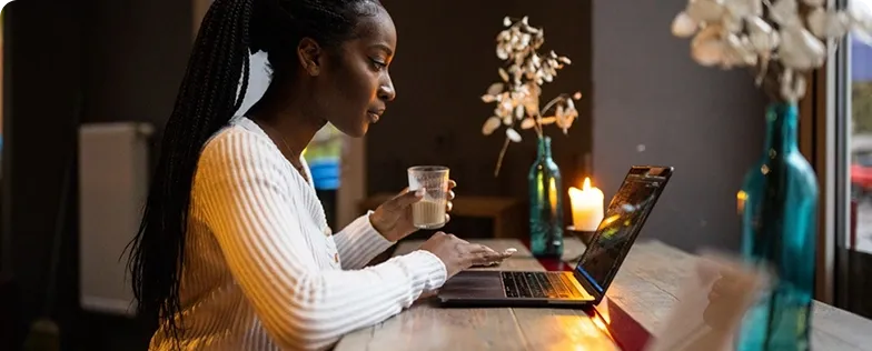 Woman holding a coffee cup while working on a laptop in a cosy café setting