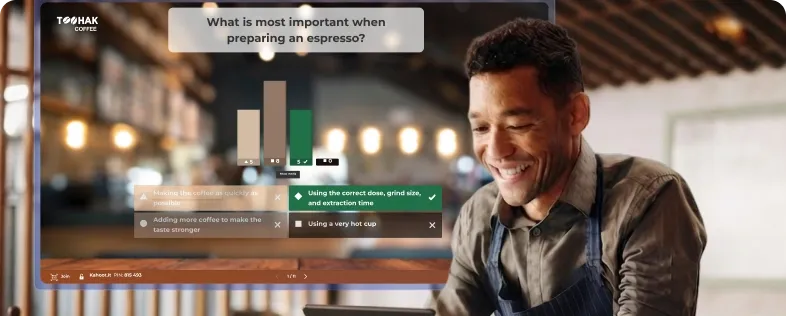 Smiling barista in an apron with a Kahoot quiz about espresso preparation displayed on screen behind him