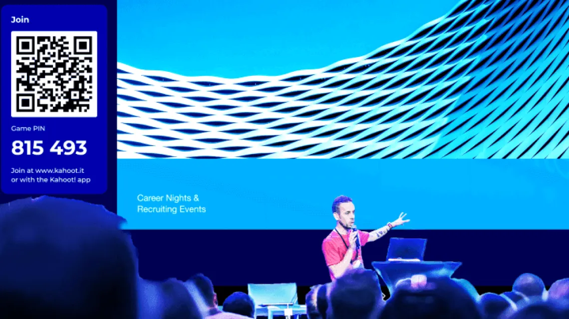 Presenter on stage at a recruiting event displaying a Kahoot game PIN and QR code on a large screen for audience to join