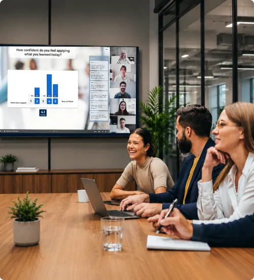 Three colleagues in a meeting room engaging with a Kahoot survey displayed on a large screen during a hybrid team session