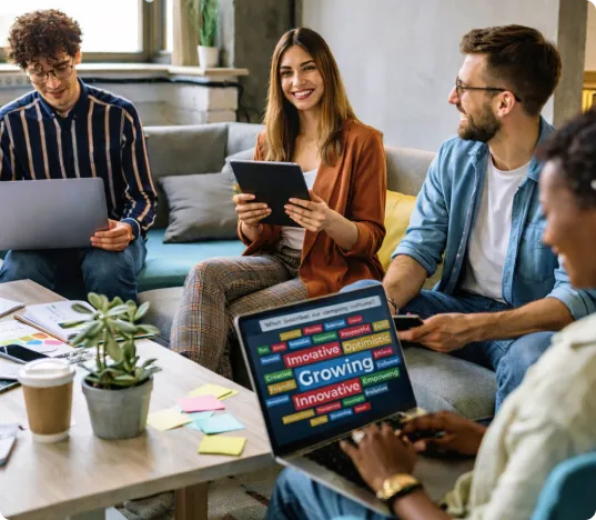 A group of four young professionals in an informal office setting. One woman in a brown blazer smiles while holding a tablet, and another person uses a laptop in the foreground displaying a Kahoot! word cloud for "What describes our company culture?" with "Growing" and "Innovative" prominently visible.