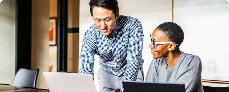 Two colleagues smiling while reviewing content together on a laptop in a meeting room