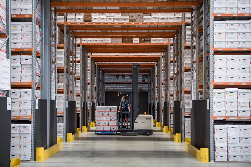A staff member is driving a bob cat with boxes in a large storage facility