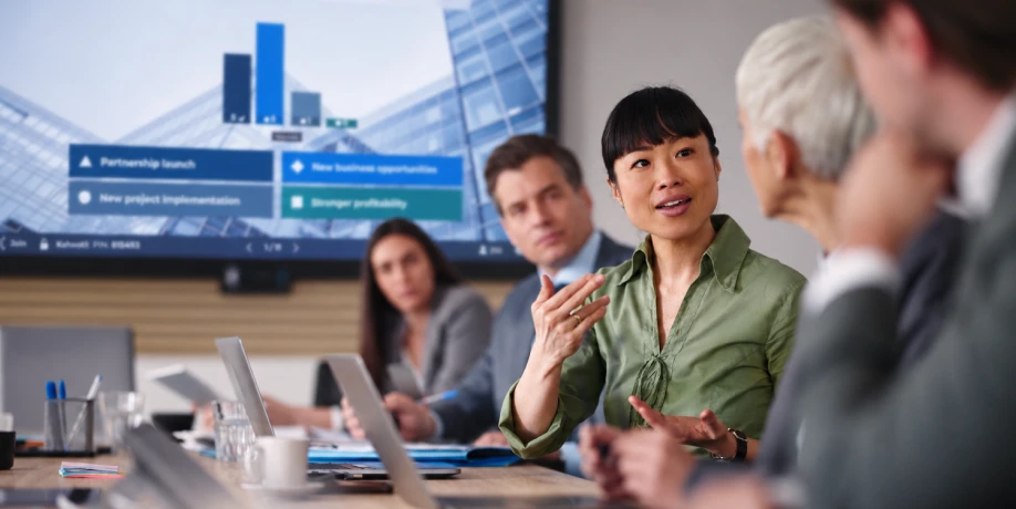 A woman speaks during a meeting while a screen behind her displays a Kahoot poll on business opportunities and priorities.