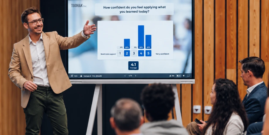 A presenter gestures toward a screen showing a bar chart poll result on confidence levels during a training session.